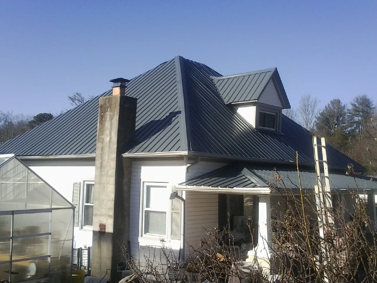 Dark blue standing seam metal roof on a white farmhouse with dormer — Slate & Tile Roof Repair by Roofing Brothers in Oakland