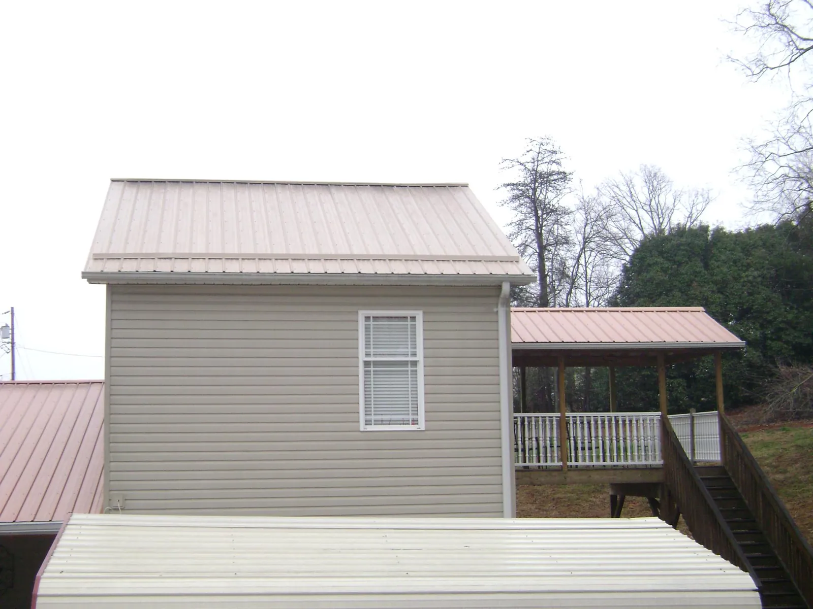 Tan metal roofs on a two story addition and attached porch, from a Roof Replacement job in Oakland